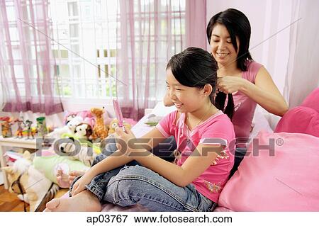 Stock Photo - Mother and daughter in bedroom, mother braiding daughters hair . Fotosearch