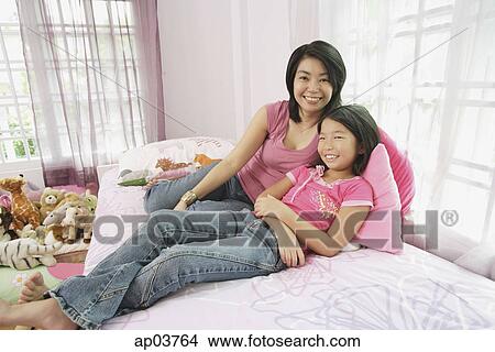 Picture - Mother and daughter in bedroom, side by side, looking at camera. Fotosearch