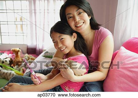 Stock Image - Mother hugging daughter, both looking at camera . Fotosearch