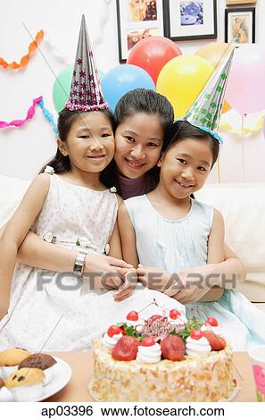 Stock Photograph - Mother with two girls celebrating a birthday, smiling at camera . Fotosearch
