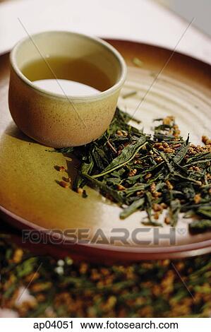 Stock Image - Tea cup on tray, tea leaves scattered around . Fotosearch