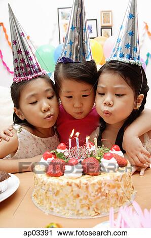 Stock Image - Three girls blowing candles on birthday cake . Fotosearch