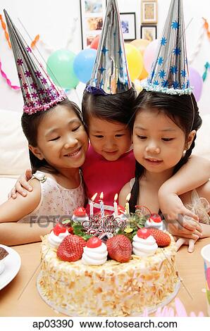Stock Image - Three girls celebrating a birthday, looking at cake. Fotosearch