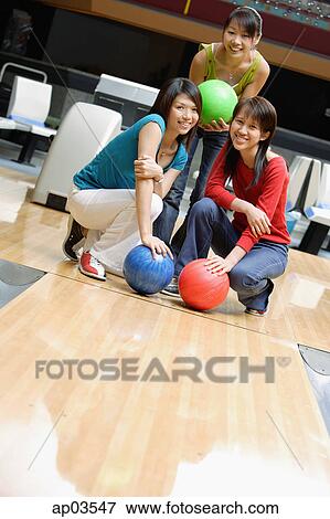 Stock Photo - Three women crouching in bowling alley, holding bowling balls . Fotosearch