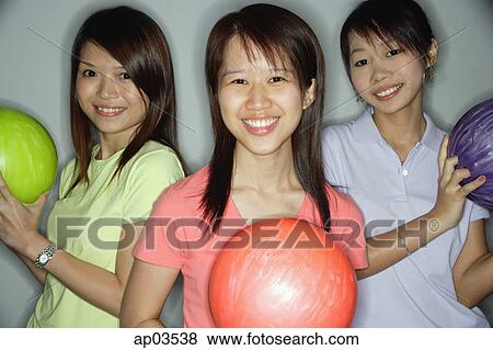 Stock Photo - Three young women holding bowling balls, smiling at camera . Fotosearch