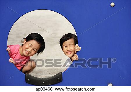 Stock Photo - Two girls in playground, looking through hole. Fotosearch