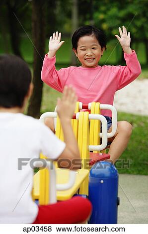 Two girls on a seesaw, raising their hands View Large Photo Image Stock Photo - Two girls on a seesaw, raising their hands. Fotosearch