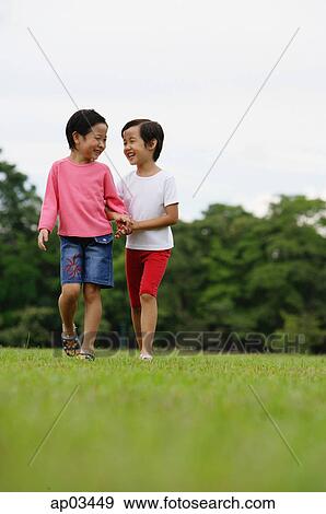 Stock Photo - Two girls on grass, walking, side by side. Fotosearch