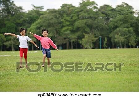 Stock Image - Two girls running on grass, side by side . Fotosearch