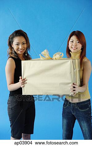 Two woman carrying big gift box, smiling View Large Photo Image Picture - Two woman carrying big gift box, smiling . Fotosearch
