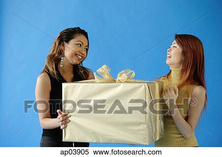 Two woman carrying big gift box, smiling at each other View Large Photo Image Stock Photography - Two woman carrying big gift box, smiling at each other . Fotosearch