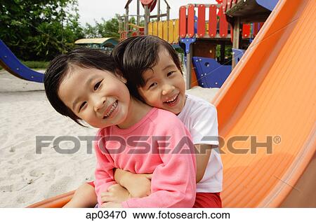 Two young girls sitting on slide, embracing, smiling at camera View Large Photo Image Stock Image - Two young girls sitting on slide, embracing, smiling at camera. Fotosearch