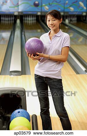 Woman at bowling alley holding bowling ball, smiling View Large Photo Image Stock Photo - Woman at bowling alley holding bowling ball, smiling . Fotosearch