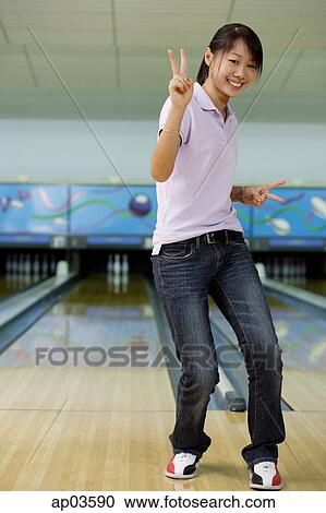 Stock Image - Woman at bowling alley, smiling, making peace sign. Fotosearch
