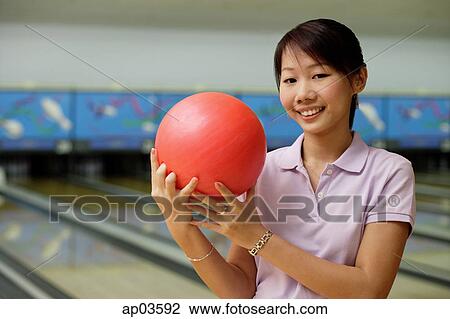 Stock Image - Woman at bowling alley, smiling, holding bowling ball. Fotosearch