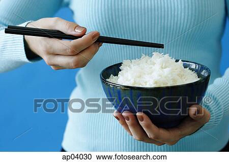 Stock Image - Woman holding bowl of rice and chopstick . Fotosearch