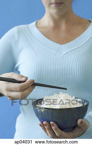 Stock Image - Woman holding bowl of rice and chopstick, cropped image . Fotosearch