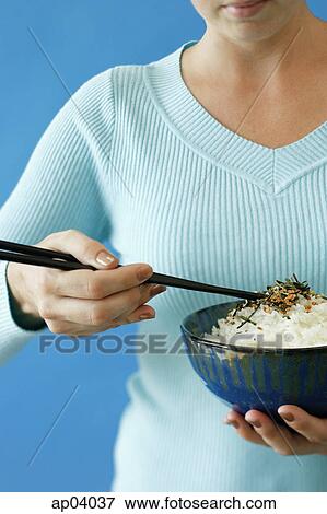 Stock Photo - Woman holding bowl of rice in one hand and chopsticks in the other. Fotosearch