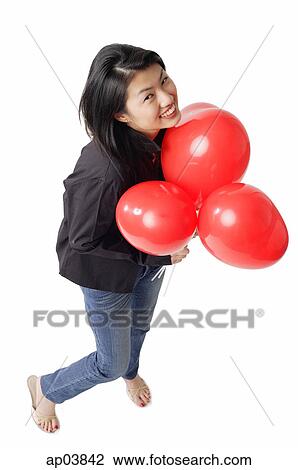 Stock Image - Woman holding red balloons, looking up, smiling . Fotosearch