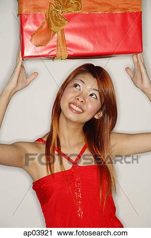 Stock Image - Woman holding red gift box over her head. Fotosearch