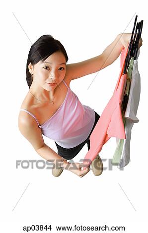 Picture - Woman holding up clothes on hangers. Fotosearch