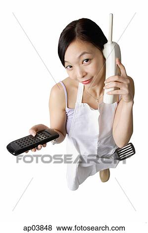 Woman in apron using cordless phone, holding remote control View Large Photo Image Stock Photo - Woman in apron using cordless phone, holding remote control. Fotosearch