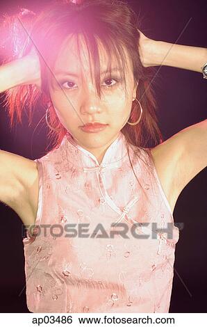 Stock Photograph - Woman in cheongsam top, hands behind head, looking at camera . Fotosearch