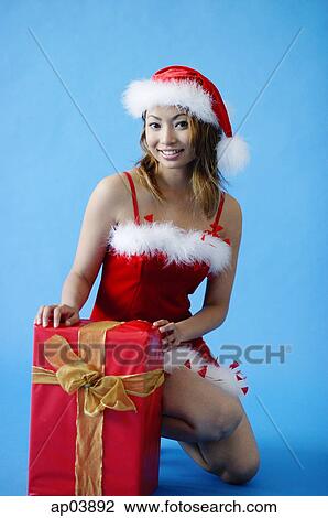 Stock Image - Woman in Santa hat, crouching next to gift box. Fotosearch