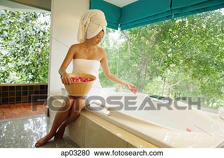 Woman in towel, sitting at edge of bath tub, throwing flower petals into tub View Large Photo Image Stock Image - Woman in towel, sitting at edge of bath tub, throwing flower petals into tub . Fotosearch