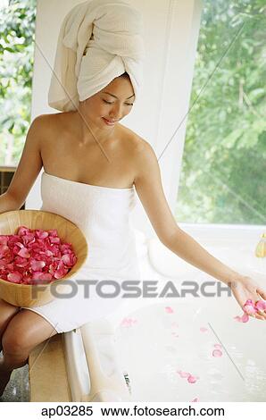 Woman in towel, sitting at edge of bath tub, throwing flower petals into water View Large Photo Image Stock Photography - Woman in towel, sitting at edge of bath tub, throwing flower petals into water . Fotosearch