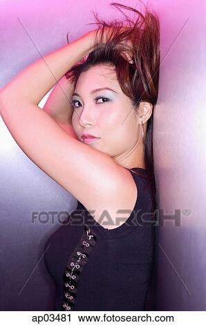 Stock Image - Woman leaning on wall, looking at camera, hands on head. Fotosearch
