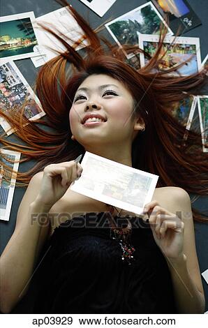 Woman lying on floor, pictures spread around her, holding postcard View Large Photo Image Stock Photo - Woman lying on floor, pictures spread around her, holding postcard . Fotosearch