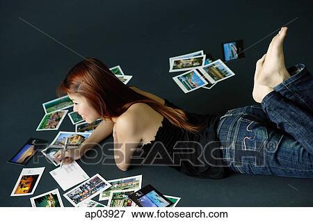 Stock Photo - Woman lying on floor, writing on backs of postcards. Fotosearch