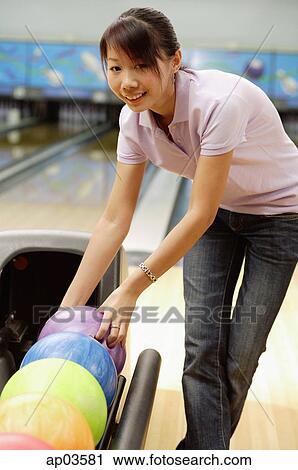 Stock Image - Woman selecting ball at bowling alley. Fotosearch