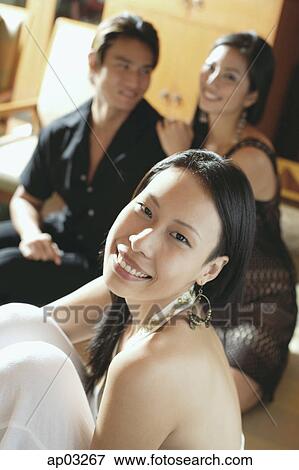 Stock Photo - Woman smiling at camera, couple in the background, smiling . Fotosearch