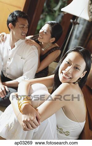 Stock Photo - Woman smiling at camera, couple in the background. Fotosearch