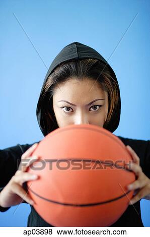Woman wearing hooded shirt, holding basketball over face View Large Photo Image Stock Photo - Woman wearing hooded shirt, holding basketball over face. Fotosearch