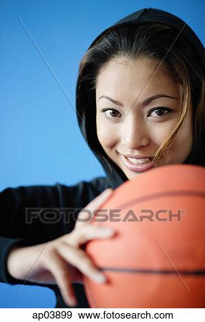 Stock Photo - Woman wearing hooded shirt, holding basketball, smiling. Fotosearch