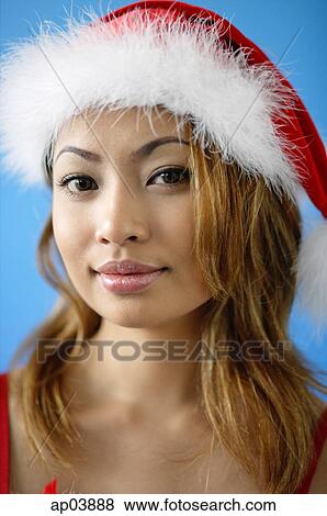 Stock Photo - Woman wearing Santa hat, looking at camera. Fotosearch