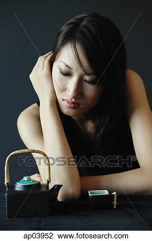 Stock Image - Woman with eyes closed, teacup and teapot next to her . Fotosearch