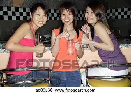Stock Photograph - Women at bar counter, holding drinks, smiling at camera . Fotosearch