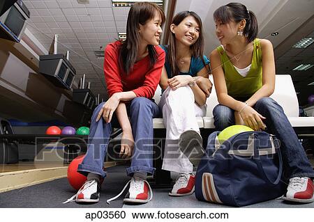 Stock Image - Women sitting side by side in bowling alley. Fotosearch