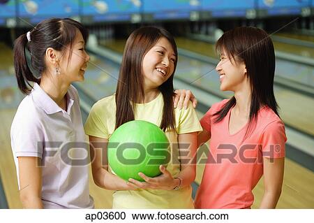 Stock Image - Women standing side by side at bowling alley, one woman holding green bowling ball. Fotosearch