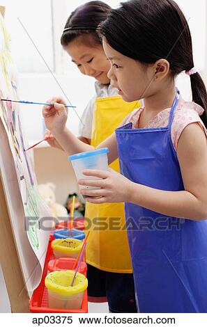 Young girls in blue and yellow aprons painting on easel View Large Photo Image Stock Photography - Young girls in blue and yellow aprons painting on easel . Fotosearch
