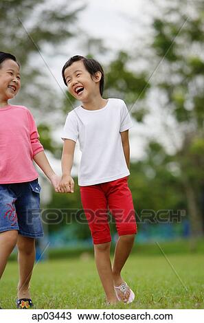 Stock Image - Young girls walking on grass, holding hands, laughing . Fotosearch