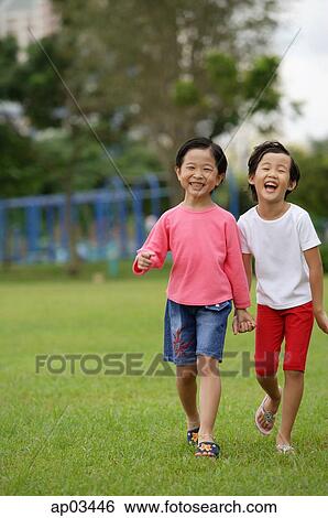Stock Photograph - Young girls walking on grass, in park, holding hands, laughing . Fotosearch
