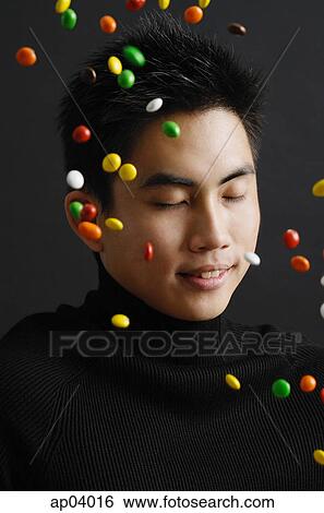 Stock Photograph - Young man dressed in black, multi coloured candy in the air around him . Fotosearch