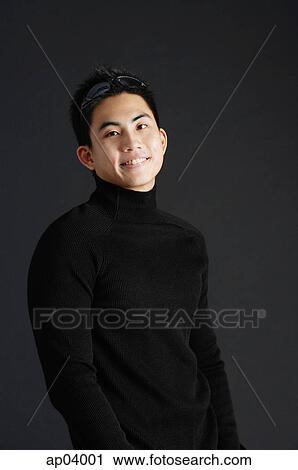 Stock Image - Young man dressed in black, standing against black background . Fotosearch