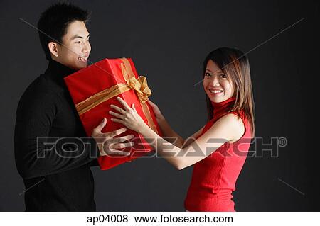 Young man giving gift to woman, woman turning to smile at camera View Large Photo Image Stock Photo - Young man giving gift to woman, woman turning to smile at camera. Fotosearch