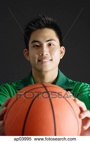 Stock Photography - Young man holding basketball, looking at camera . Fotosearch